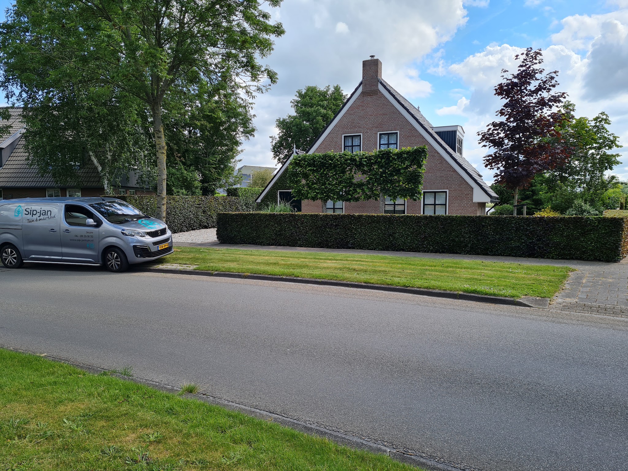 De bus van Sip-jan Tuin en onderhoud geparkeerd langs een strak geschoren beukenhaag in Joure