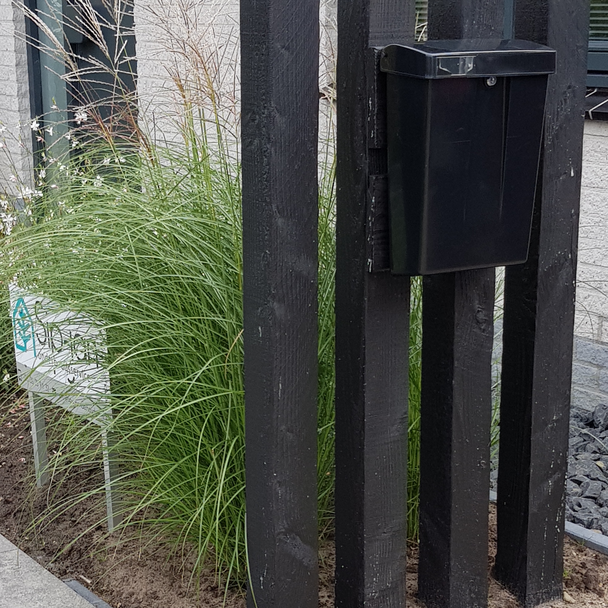 Tuindetail met zwarte houten palen, brievenbus en hoge siergrassen in bloei