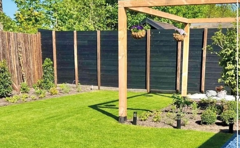 Aangelegde achtertuin met nieuw gras, houten pergola, donkere schutting en een pad van blauwe split